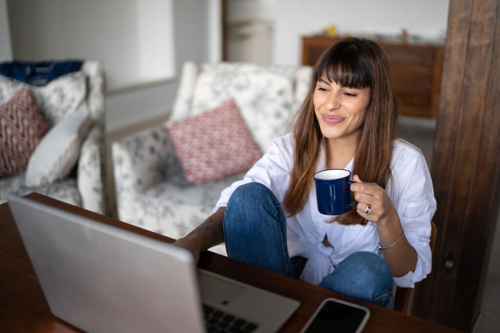 Young woman using the laptop and drinking coffee at home