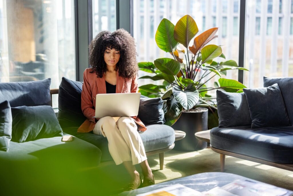 Young African woman working on laptop sitting at office lobby